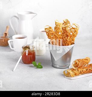 Ein Stapel gerollter Pfannkuchen sarang mit einem Glas Marmelade und Tassen Tee auf einem Marmortisch. Leckeres Frühstück. Süßes Dessert. Selektiver Fokus Stockfoto