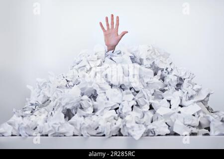 Helfen Sie mir, im Papierkram zu ertrinken. Eine Hand, die unter einem Stapel Papiere nach oben greift. Stockfoto