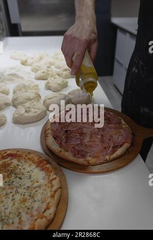 Der Koch gießt Olivenöl auf eine Pizza im Restaurant Stockfoto