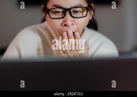 Gähnende und schläfrige Frau, die zu Hause im Büro an einem Notebook arbeitet. Müde Geschäftsfrau mit Brille, die ihren Laptop im Büro benutzt und recherchiert Stockfoto