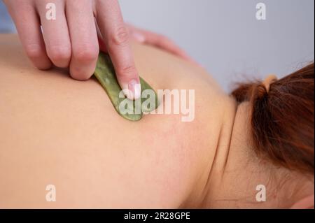 Der Masseur macht eine Rückenmassage mit einem Gouache-Schaber für eine weibliche Klientin. Stockfoto