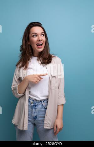 Überraschend emotionale Brünette 30-jährige Frau, die in Hemd und Jeans gekleidet ist, sieht auf blauem Hintergrund weg Stockfoto