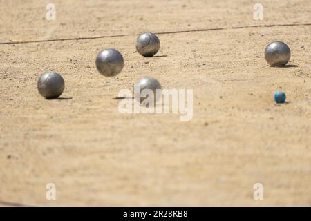 Metallball aus dem Petanque-Spiel, der sich der Bowlingkugel nähert, die auf dem sandigen Boden prallt und an einem sonnigen Tag Staub von einem Petanque-Platz erhebt Stockfoto