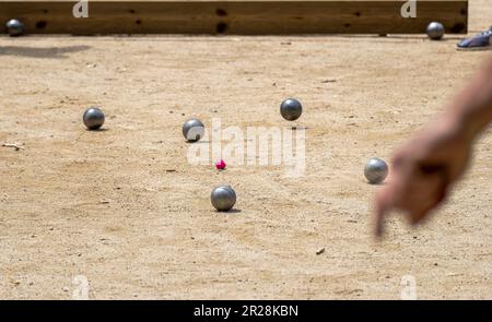 Silhouette der Hand nach dem Wurf des Petanque-Balls auf der sandigen Strecke, um ihn an einem sonnigen Sommertag dem bloche näher zu bringen Stockfoto