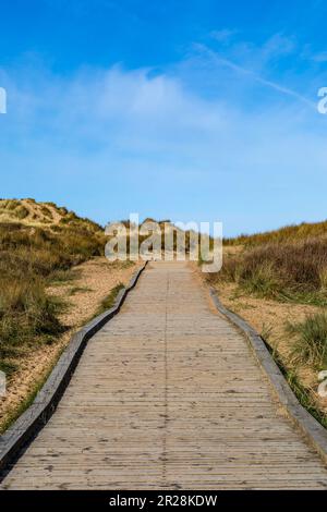 An einem sonnigen Morgen blickte man auf einem hölzernen Fußweg durch Sanddünen in Richtung Strand Stockfoto