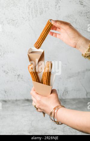 Eine Frau, die Churros aus einer Dose nimmt und sie in Schokoladensoße taucht Stockfoto