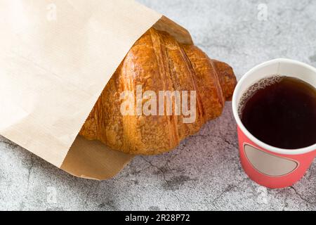 Croissant eingewickelt in Geschenkpapier und neben Tee auf einem Steintisch Stockfoto