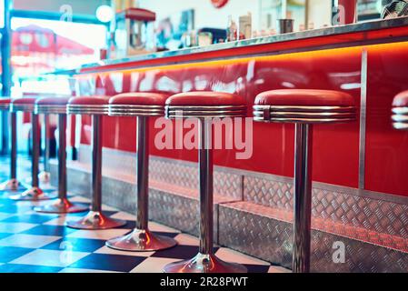 Trendige Einrichtung im Vintage- und Retro-Stil in einem Diner, Restaurant oder einer Cafeteria mit flippigem Dekor. Sitzecke, alte Schule und Stühle an einer Theke oder Bar in einem Groovy Stockfoto