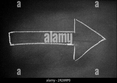Weißer Pfeil auf einer schwarzen Tafel mit Kreide, der eine Richtung angibt Stockfoto
