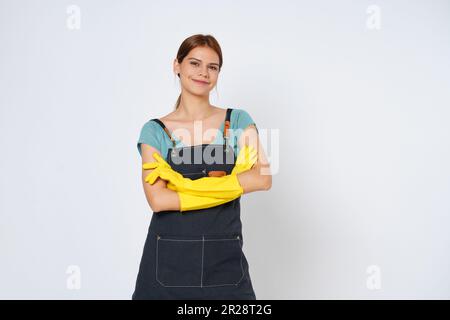Junge Frau mit gelben Gummihandschuhen, die mit gekreuzten Armen auf weißem Hintergrund steht. Stockfoto