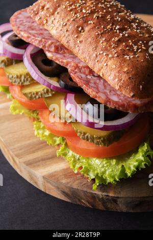 Sandwich mit gesalzener Gurke, Tomaten, Salat, Oliven und Zwiebeln auf einem Holzbrett Stockfoto