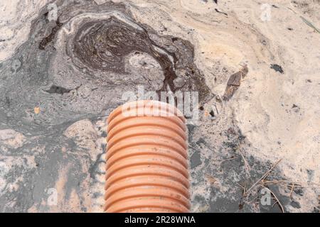 Abflussrohr mit fließendem Wasserstrom. Sturmwassermanagement in öffentlichen Räumen, Kunststoffrohren, Steinen und Sträuchern. Plastikrohre für die Naht Stockfoto