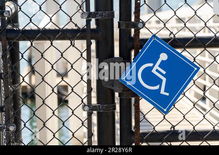 Ein schwarzes Metallzauntor mit Kettenglied und einem Hinweisschild für Fallbehinderte. Stockfoto