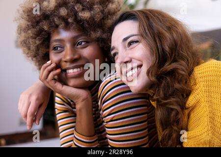 Nahaufnahme eines wunderschönen, multirassischen Paares, das sich umarmt und entspannt. Portrait zweier multiethnischer lächelnder junger Frauen, die kuscheln. Stockfoto