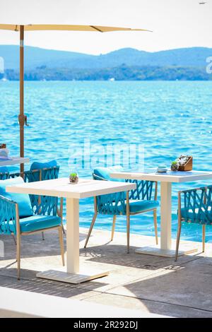 Beach Club Konzept. Das Hotel verfügt über eine stilvolle Essecke oder ein Strandcafé am Meer. Restauranttische, strohhaltige Naturstühle, weiße Holztische, mak Stockfoto