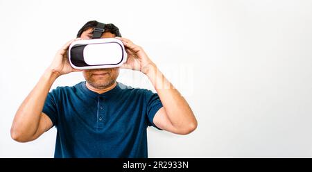 Ein lächelnder Mann, der mit beiden Händen Virtual Reality (VR) in Weiß und Schwarz hält. Der junge Mann war glücklich, als er sich ein Tutorial anschaute, wie man Sport treibt Stockfoto