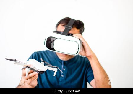 Ein Einzelgänger hält eine Drohne und spielt VR, um die Drohne zu bedienen. Der junge Mann war glücklich, als er sich ein Tutorial zum Fliegen mit VR anschaute. Virtueller Real Stockfoto