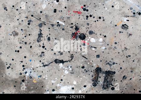 Der Boden ist mit mehreren Tropfen in verschiedenen Farben befleckt. Tropfende Farbe auf dem Betonboden wunderschöne Kunst. Tröpfchen mit roten, schwarzen und weißen Flecken Stockfoto