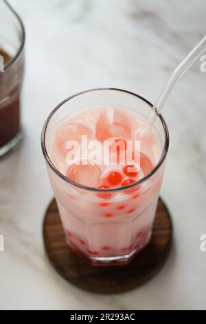 Nahaufnahme von hausgemachtem Milchblasentee mit Tapiokapperlen. Erdbeermilch-Teegetränk mit Tapiokasseln. Eisgekühltes milchiges Getränk mit Tapioka-Blasen und Eis Stockfoto