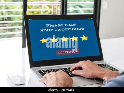 Auf dem Laptop-Bildschirm wird die Meldung Bitte bewerten Sie Ihre Erfahrung angezeigt, um die Zufriedenheit mit dem Service zu bestätigen. Ein Mann sitzt und tippt zu Hause bei der Arbeit die Tastatur. Konz Stockfoto
