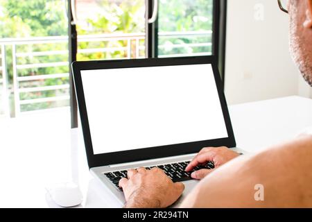 Nahaufnahme, Leute arbeiten zu Hause Blogger. Ein Mann sitzt und tippt ein Dokument mit einem Laptop auf einem weißen Tisch im Wohnzimmer zu Hause. Der weiße Bildschirm ist bla Stockfoto
