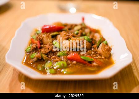 Scharfes Curry mit Garnelenpaste und Garnelenpaste auf einem weißen Teller auf einem Holztisch. Meeresfrüchte sind bei Thailändern sehr beliebt. Nahaufnahme und Steigung Stockfoto