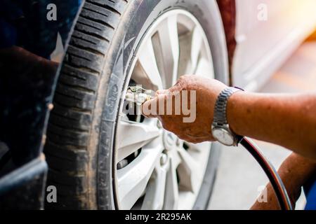 Die Hand eines jungen Mannes, der das Rohr hält, um den Luftdruck zu prüfen und die Stickstoffluft in den Reifen seines Autos in einer Tankstelle zu füllen, nehmen Sie die Nähe Stockfoto