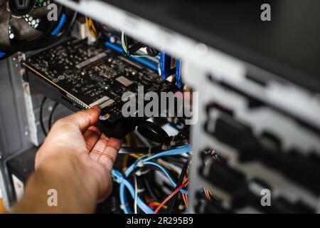 Die Hand eines Technikers hält die Grafikkarte, um sie zu reparieren. Die VGA-Karte ist beschädigt und verursacht einen Computerfehler. Die Displaykarte zeigt keinen PC sc an Stockfoto
