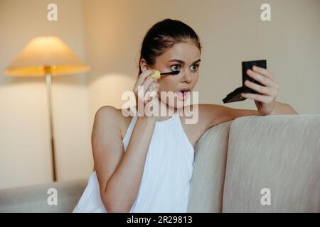 Eine Frau zu Hause schaut in den Spiegel und trägt Make-up-Farbstoff Mascara Wimpern, Schönheitskonzept, Pflege für Problemhaut mit Akne. Hochwertiges Foto Stockfoto