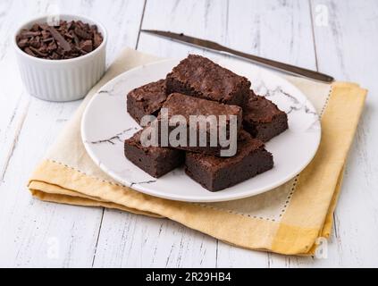 Brownies auf einem Teller mit Schokoladenstückchen auf einem weißen Holztisch. Stockfoto