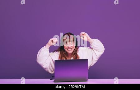 Weibliche Gamer, die ein Online-Videospiel in einem Studio gewonnen hat. Glückliche junge Frau, die einen interaktiven Streaming-Dienst auf ihrem Laptop nutzt. Stockfoto
