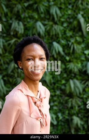 Porträt einer fröhlichen afroamerikanischen Fachfrau mit kurzen Haaren, die gegen Pflanzen steht Stockfoto