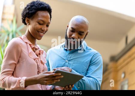 Low-Angle-Ansicht afroamerikanischer Kollegen, die außerhalb des Büros über ein digitales Tablet diskutieren Stockfoto