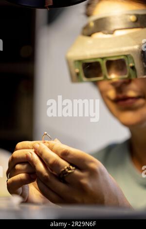 Eine Kaukasierin, die eine Schutzbrille trägt und Schmuck in der Schmuckwerkstatt anschaut Stockfoto