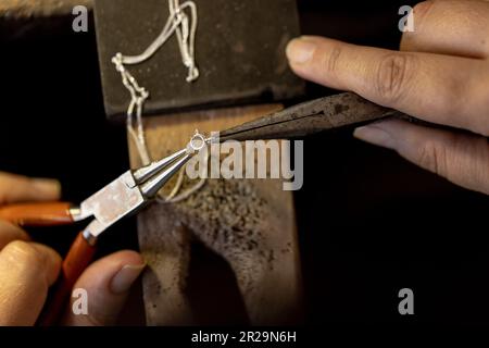 Nahaufnahme der Hände einer birassischen Arbeiterin, die Schmuck mit Werkzeugen in einer Schmuckwerkstatt herstellt Stockfoto