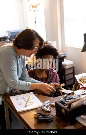 Verschiedene Mitarbeiter, die Schmuck mit Werkzeugen herstellen und in einer Schmuckwerkstatt miteinander sprechen Stockfoto