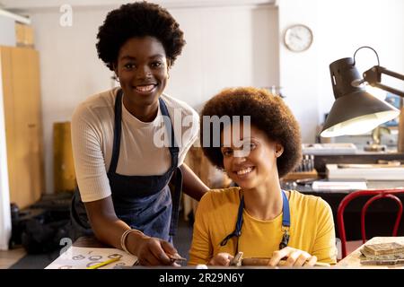 Porträt von glücklichen, vielfältigen Arbeitern, die Schmuck mit Werkzeugen herstellen und in der Schmuckwerkstatt lächeln Stockfoto