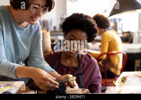 Zufriedene, vielfältige Mitarbeiter, die Schmuck mit Werkzeugen herstellen und sich in der Schmuckwerkstatt unterhalten Stockfoto