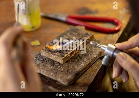 Nahaufnahme der Hände einer birassischen Arbeiterin, die Schmuck mit Werkzeugen in einer Schmuckwerkstatt herstellt Stockfoto