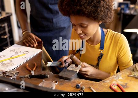 Zufriedene, vielfältige Mitarbeiter, die in der Schmuckwerkstatt Schmuck mit Werkzeugen herstellen Stockfoto