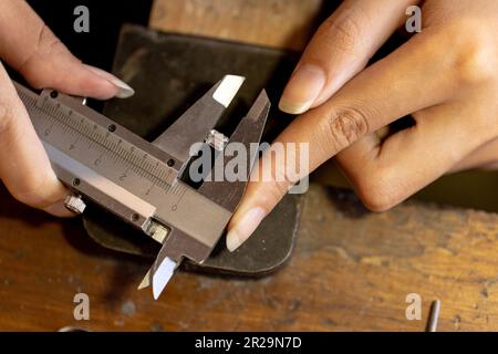 Nahaufnahme der Hände einer birassischen Arbeiterin, die Schmuck mit Werkzeugen in einer Schmuckwerkstatt herstellt Stockfoto