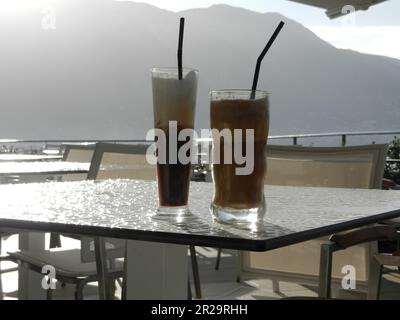 Nahaufnahme von zwei kalten Kaffees auf einem Glastisch mit Bergen im Hintergrund in Griechenland Stockfoto