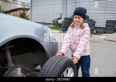 Ein Kind im Autodienst, beim Reifenwechsel und beim Kundendienst des Fahrzeugs. Auto-Reparaturkonzept Stockfoto