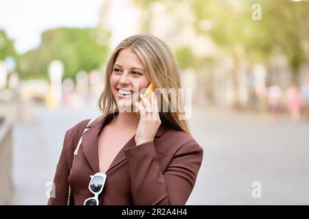 Schöne junge blonde Frau, die lächelt, während sie ein Telefongespräch führt Stockfoto