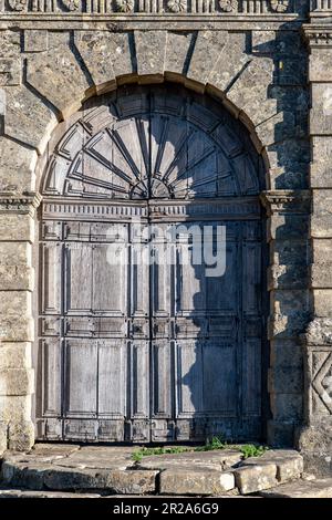 Nahaufnahme der ummauerten Fassade eines Herrenhauses mit verwitterter Holzeingangstür und Ornamenten am Steineingang entlang des öffentlichen Fußwegs in der Nähe des Cotswold Way Stockfoto