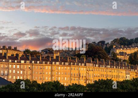 Blick aus dem niedrigen Winkel auf eine lange Reihe charakteristischer Stadthäuser mit Dächern und Schornsteinen georgianischer Häuser in Bath, Sommerset, Großbritannien, in leuchtendem Orange Stockfoto