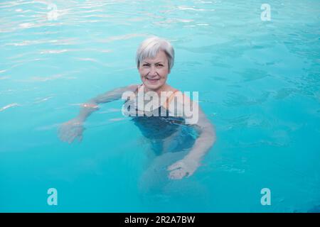 Seniorin im Swimmingpool mit warmem Wasser aus Thermalquellen. Porträt einer aktiven älteren Kaukasierin mit grauen kurzen Haaren im lächelnden Badeanzug Stockfoto