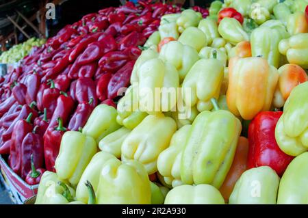 Nahaufnahme eines Stapels roter, grüner und gelber Paprika an einem Marktstand. Stockfoto