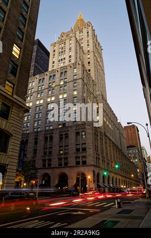 Am frühen Morgen führt der Verkehr Lichtpfade am New York Life Building vorbei, wenn die Morgendämmerung eintrifft. Stockfoto