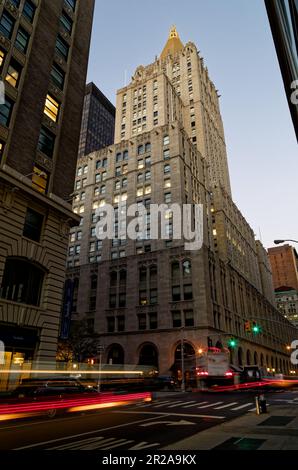 Am frühen Morgen führt der Verkehr Lichtpfade am New York Life Building vorbei, wenn die Morgendämmerung eintrifft. Stockfoto